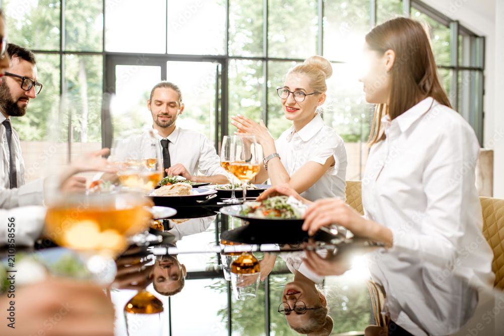 Business people dressed in white shirts having fun sitting together during a business lunch with delicious meals and wine in the modern restaurant Business people dressed in white shirts having fun sitting together during a business lunch with delicious meals and wine in the modern restaurant