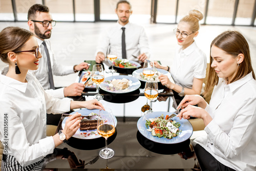 Business people dressed in white shirts having fun sitting together during a business lunch with delicious meals and wine in the modern restaurant