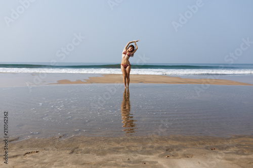 In the background, waves splash in the ocean. The sea horizon. The girl in the swimsuit is pleased with the rest, spreading her hands to the side. The concept of freedom. Pure consciousness. Joy.
