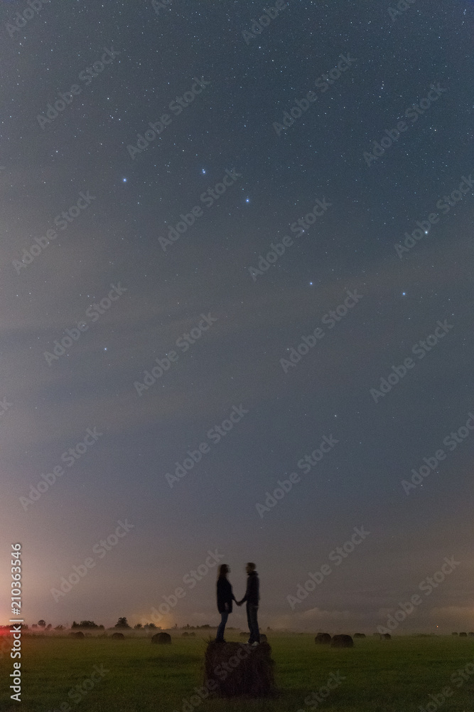 Young girl and boy staying on the haystack and watching the stars in the sky. Romantic