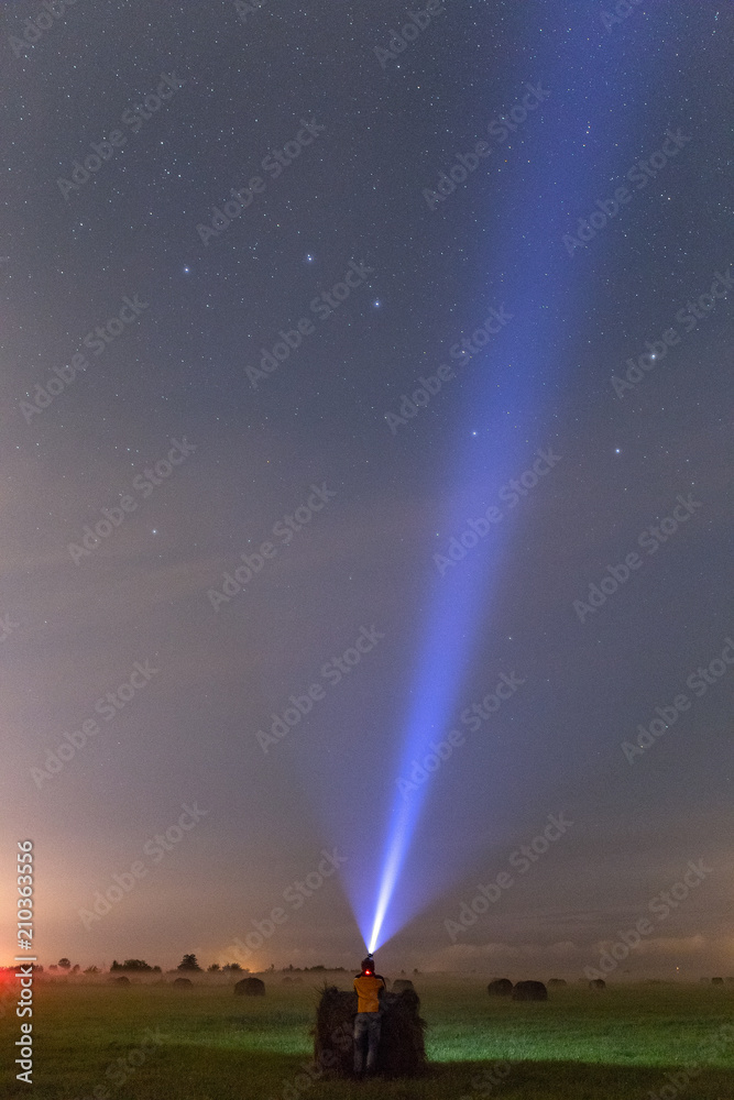 A man staying near the haystack in the green field at night. Light ray pointing to stars A man staying near the haystack in the green field at night. Light ray pointing to stars