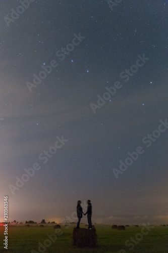 Fototapeta Naklejka Na Ścianę i Meble -  Young girl and boy staying on the haystack and watching the stars in the sky. Romantic