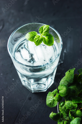 Cocktail wather with ice and mint in a glass on black background. Summer refreshing drink.