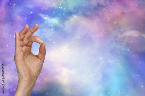 Our Perfect Universe - female hand with index finger touching thumb making OK sign against a beautiful colourful cosmic heavenly sky with copy 
