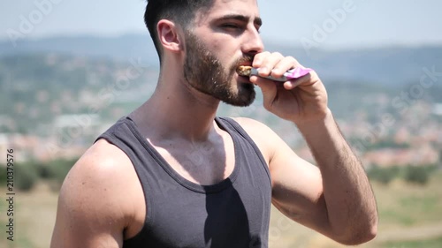 Young muscular man eating protein bar outdooron a balcony in summer