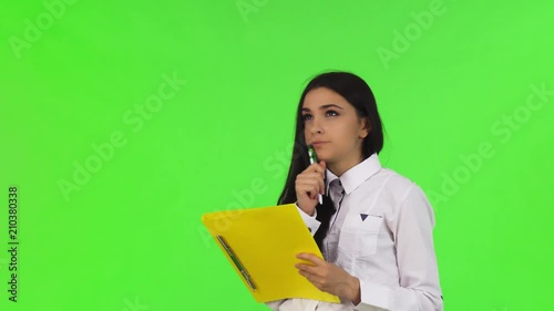 Studio portrait of a beautiful dark haired young businesswoman doing paperwork, looking away thougthfully. Attractive female worker filling documents on her clipboard. Employment concept. photo