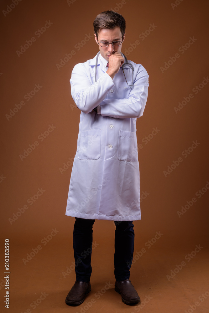 Young handsome man doctor against brown background Young handsome man doctor against brown background