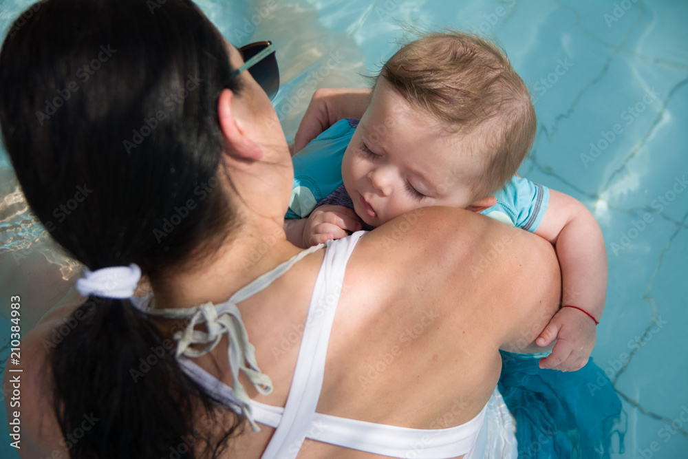 Closeup portrait of cute little baby sleeping on mothers shoulder in the pool, happy young loving family, new life concept Closeup portrait of cute little baby sleeping on mothers shoulder in the pool, happy young loving family, new life concept