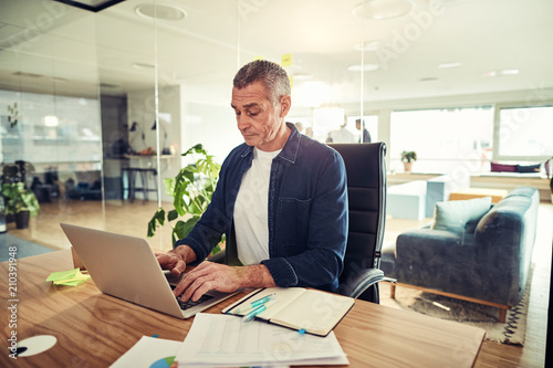 Businessman sitting at his office desk working on a laptop photo