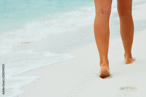 Fototapeta Naklejka Na Ścianę i Meble -  Beach travel - woman walking on sand beach leaving footprints in the sand. Closeup detail of female feet