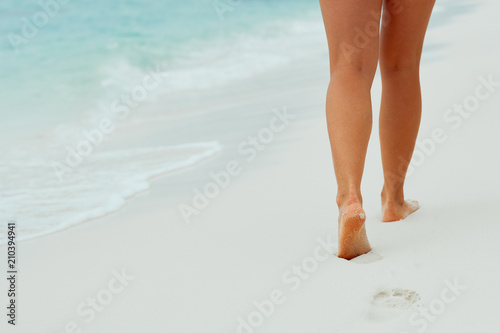 Woman walking on sand beach leaving footprints in the sand. Сlose up of woman leg on the beach.