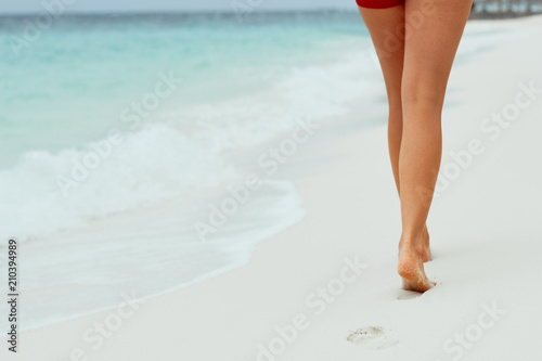 Beach travel - woman walking on sand beach leaving footprints in the sand. Closeup detail of female feet