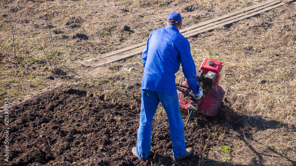 Worker with a machine cultivator digs the soil in the garden Worker with a machine cultivator digs the soil in the garden