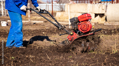 Worker with a machine cultivator digs the soil in the garden