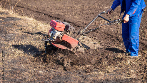 Worker with a machine cultivator digs the soil in the garden