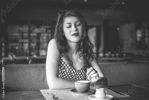 Fashion retro style portrait of young beautiful woman in polka dot dress.   Retro (vintage) portrait of the alluring young girl sitting in cafe. Pin up style portrait of young girl in dress 