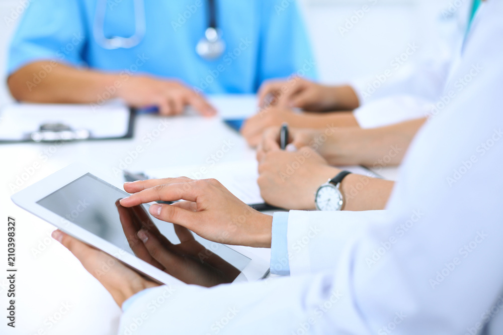 Doctor using tablet computer at medical meeting, closeup. Group of colleagues at the background Doctor using tablet computer at medical meeting, closeup. Group of colleagues at the background