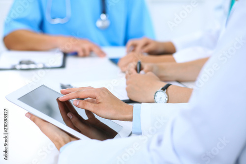 Doctor using tablet computer at medical meeting, closeup. Group of colleagues at the background