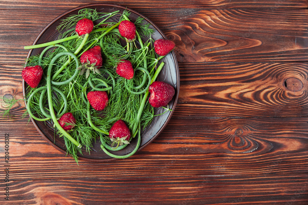 Strawberries and greens on a brown plate on wooden background. Copy space Strawberries and greens on a brown plate on wooden background. Copy space