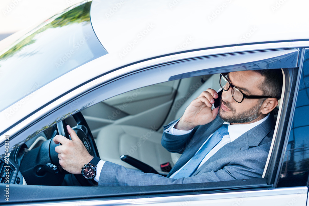 side view of businessman in eyeglasses talking on smartphone while driving car side view of businessman in eyeglasses talking on smartphone while driving car