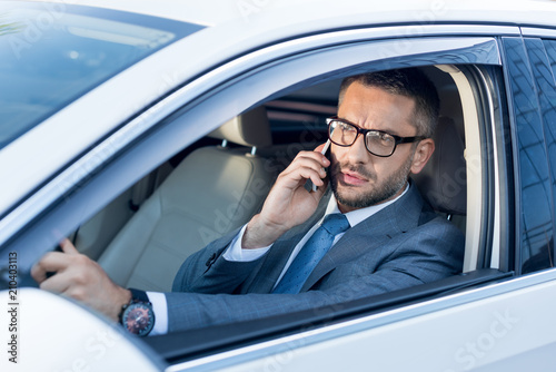 portrait of businessman in eyeglasses talking on smartphone while driving car