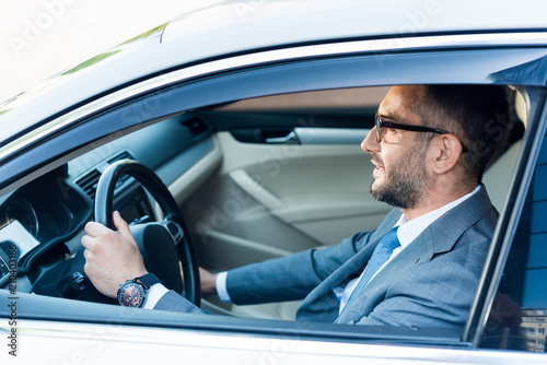 side view of businessman in suit and eyeglasses driving car alone