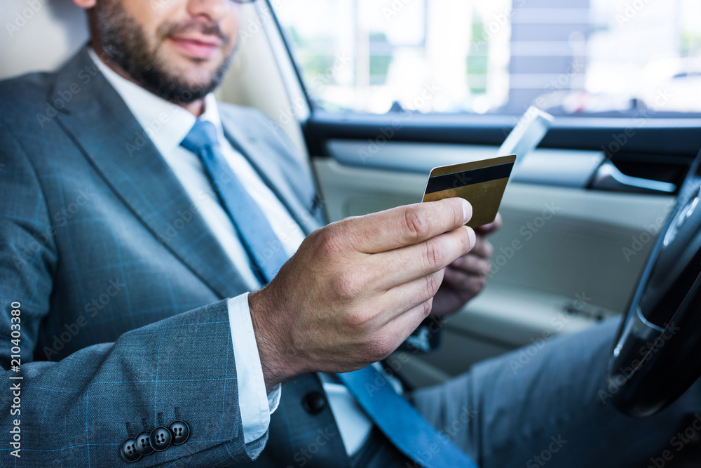partial view of businessman with tablet and credit card sitting in car partial view of businessman with tablet and credit card sitting in car