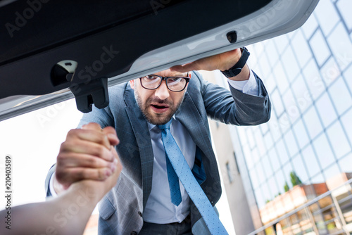partial view of businessman holding hand of man in luggage boot of car