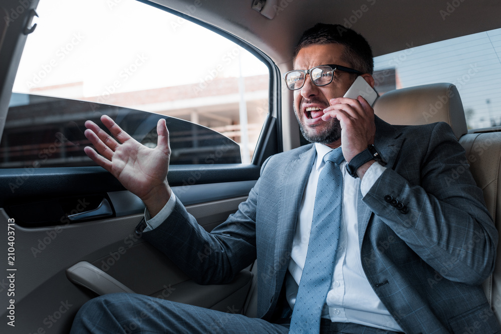 emotional businessman talking on smartphone while sitting on backseat in car