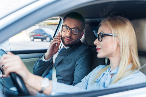 selective focus of businesswoman driving car while colleague talking on smartphone near by on passengers seat © LIGHTFIELD STUDIOS
