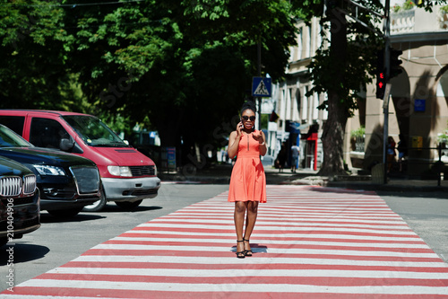 Stylish african american woman walking on crosswalk or pedestrian crossing and speaking on mobile phone. © AS Photo Family