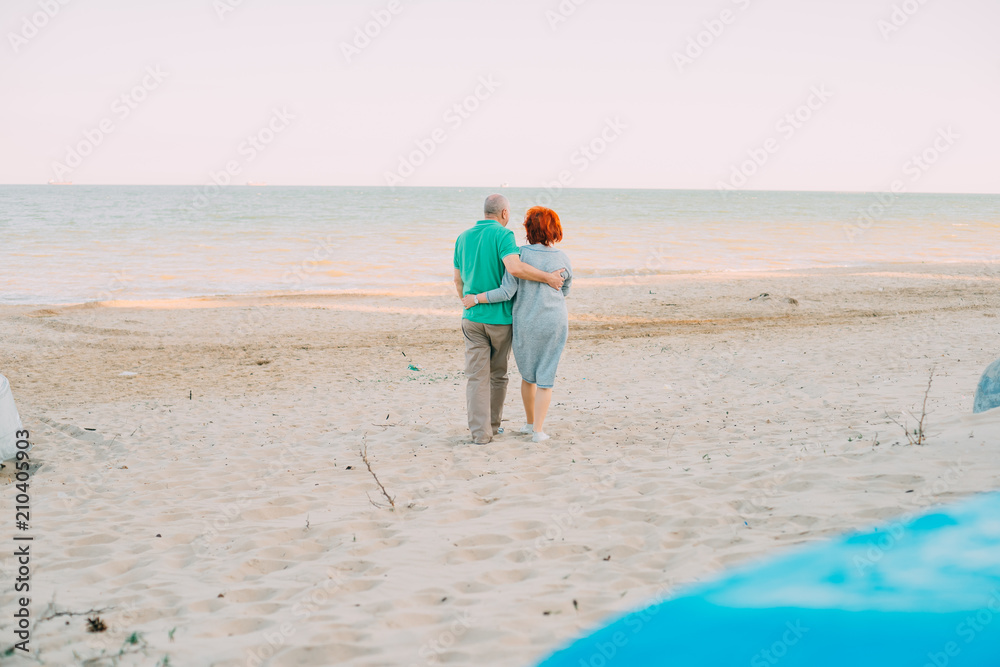 Outdoor shot of romantic senior couple walking along the sea shore holding hands. Senior man and woman walking on the beach together
