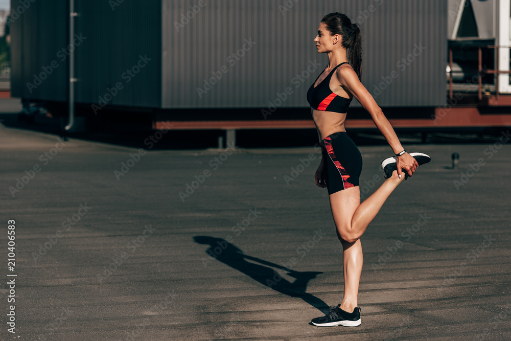 young sportswoman stretching legs on roof in city young sportswoman stretching legs on roof in city