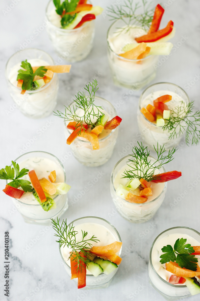 Snack in a glass with fresh cream and various vegetables on a light background.