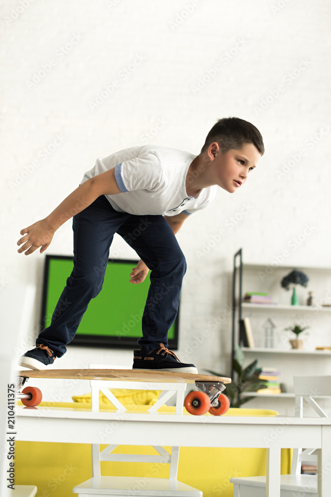 Obraz premium pre-adolescent boy standing on skateboard on table at home