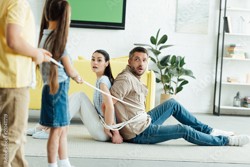 cropped image of children tying parents with rope on floor at home