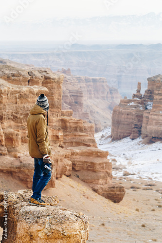 A cheerful traveler with a camera stands on the edge of the cliff in the Charyn canyon in Kazakhstan. Analogue of the American Grand Canyon.