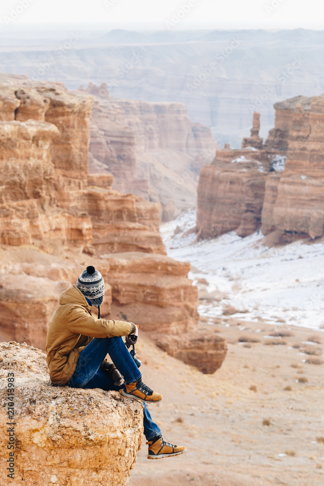 A cheerful traveler with a camera sits on the edge of a cliff in the Charyn canyon in Kazakhstan. Analogue of the American Grand Canyon.