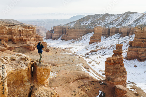 A cheerful traveler with a camera stands on the edge of the cliff in the Charyn canyon in Kazakhstan. Analogue of the American Grand Canyon.