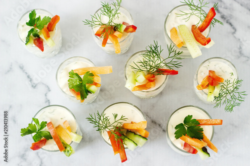 Snack in a glass with fresh cream and various vegetables on a light background.