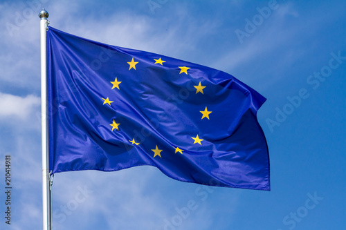 Flag of the European Union waving in the wind on flagpole against the sky with clouds on sunny day, close-up photo