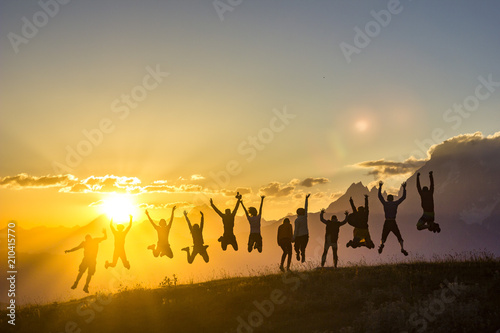 group of people with hands up jumping on grass in sunset mountains