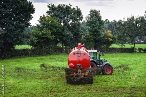 Farmer spraying liquid manure by use of a slurry tanker on a green meadow.  photo