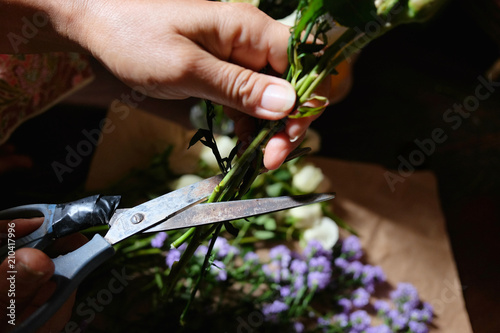 Close up on hands of woman working on a bouquet of flowers in a vase.Florist woman decorate White roses and Purple Marguerite Daisy flowers on wooden table.People and floral arrangement concept.q photo