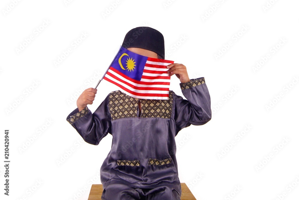 Young Malay Asian boy wearing Malay traditional clothe baju melayu with skull cap or songkok holding and waving Malaysia flag isolated on white Young Malay Asian boy wearing Malay traditional clothe baju melayu with skull cap or songkok holding and waving Malaysia flag isolated on white
