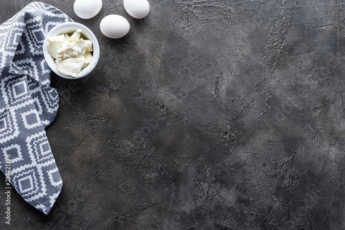 top view of arranged raw chicken eggs, sour cream in bowl and linen on dark grey tabletop