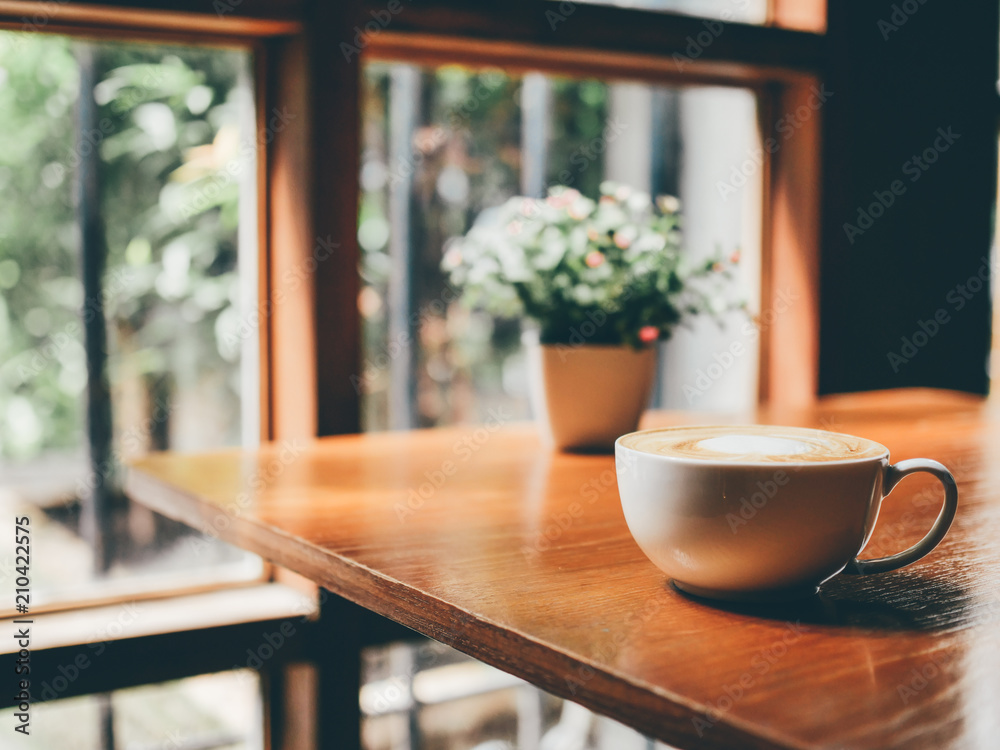 A hot coffee cup  on wooden table with beautiful sunlight from the windows.
