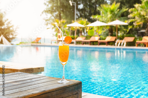 Photography Orange juice glass on wooden table with swimming pool view background