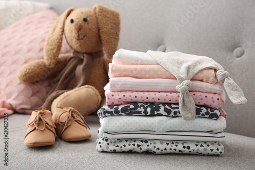 Toy bunny, stack of stylish child clothes and shoes on sofa © New Africa