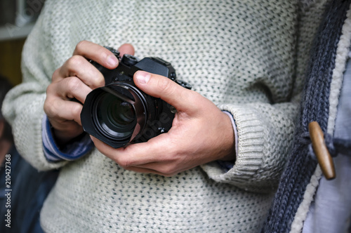 A man in a knitted sweater is holding a camera in his hands, close-up.